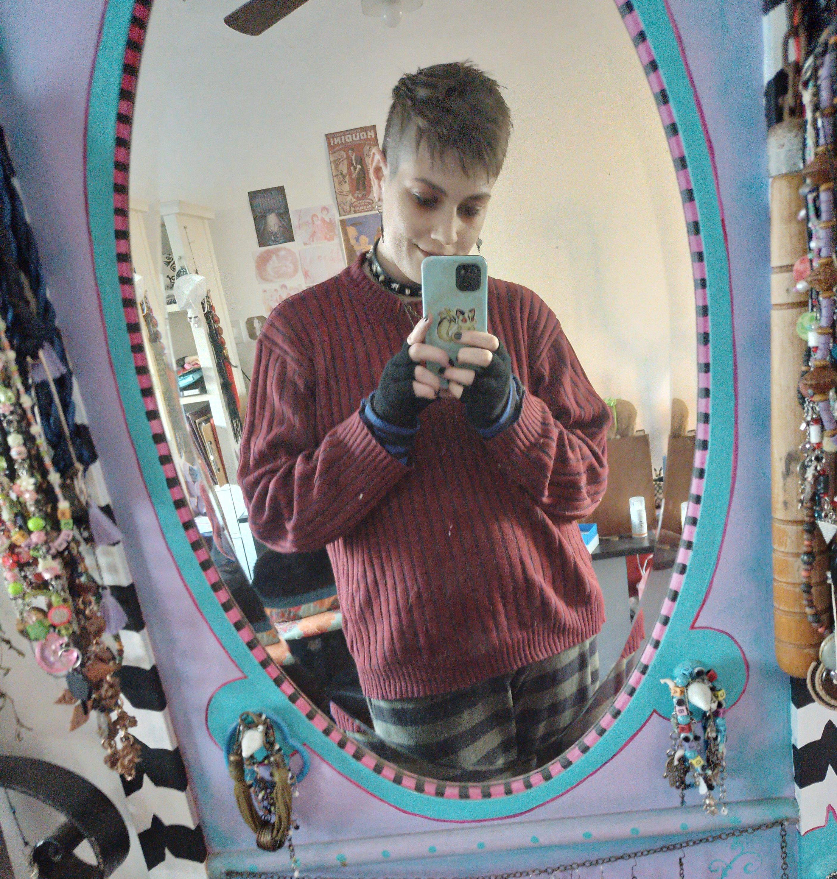 Mirror selfie, nonbinary person with short hair and spiked choker. The mirror's border is painted in pastel color.